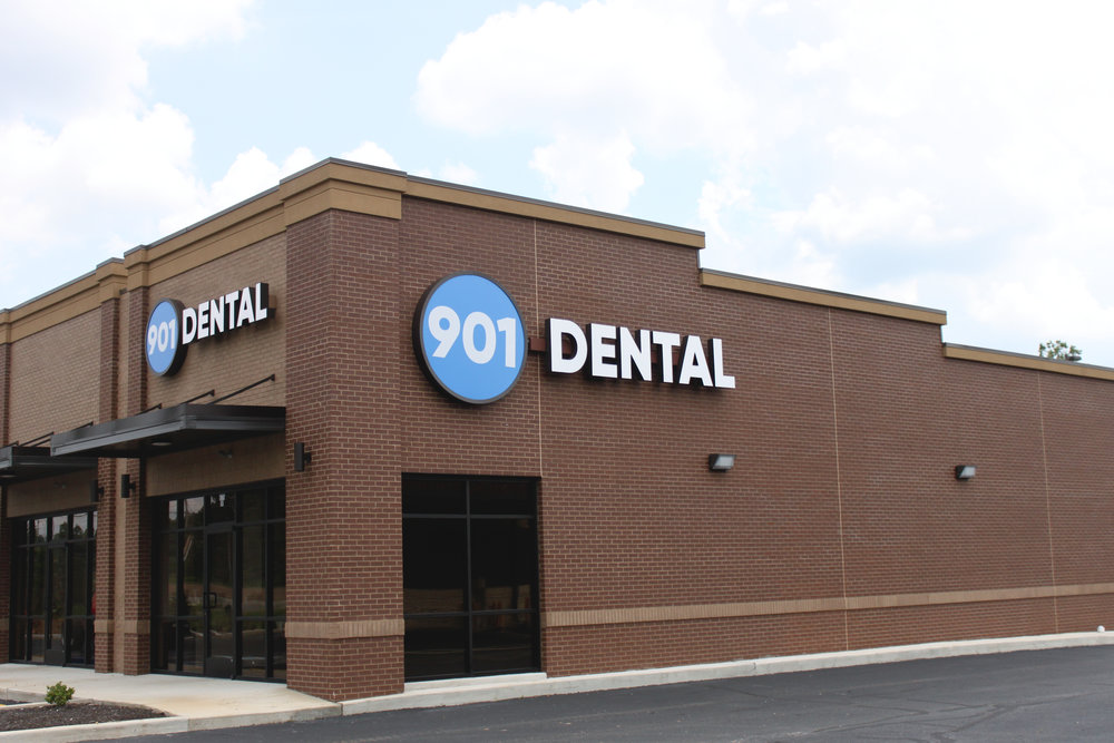 Exterior of 901 Dental clinic, brick building with blue illuminated signage and entrance doors.