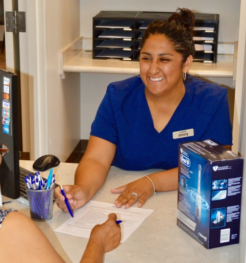 Dental professional in blue scrubs writing at desk in modern dental office setting.