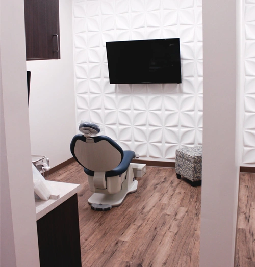 Modern dental office operatory with chair, mounted monitor, and white textured wall paneling.
