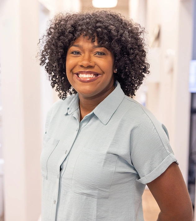 Smiling woman in light blue shirt poses for professional headshot in dental office setting.