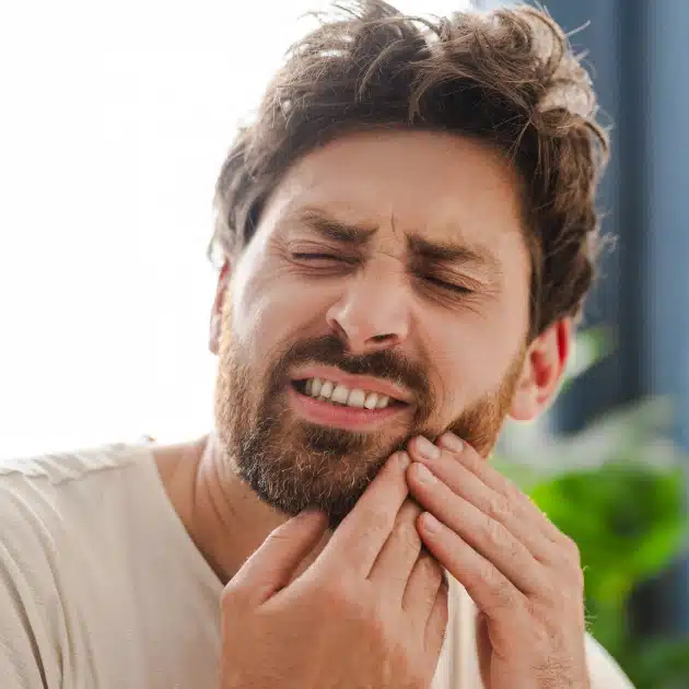 Man holding jaw in pain, displaying tooth discomfort outdoors during daytime.